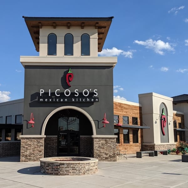 Picoso's Mexican Kitchen exterior with a prominent sign, arched entrance, and outdoor fire pit.