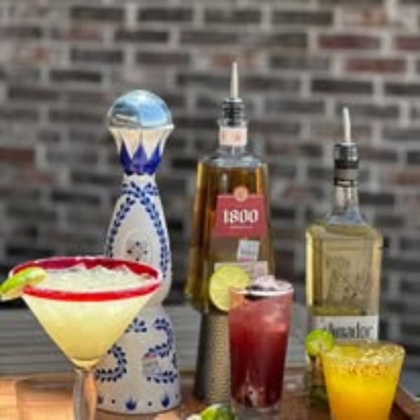 Three Picoso's Mexican Kitchen cocktails and two tequila bottles on a wooden surface.