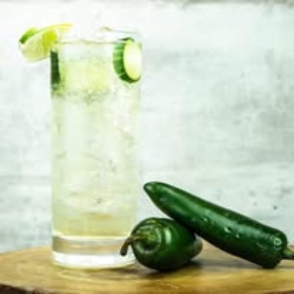 Tall glass of clear Picoso's Mexican Kitchen drink with lime and cucumber, next to two jalapeños.