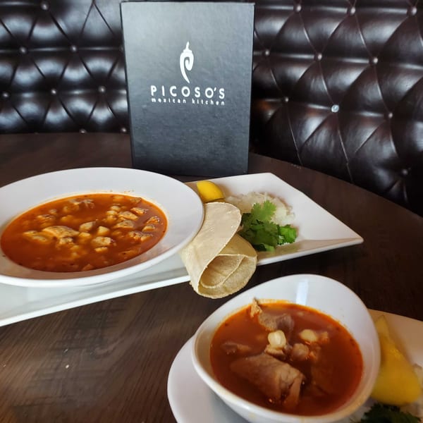 Two bowls of Picoso's Mexican Kitchen pozole with tortillas, cilantro, onions, and lemon.