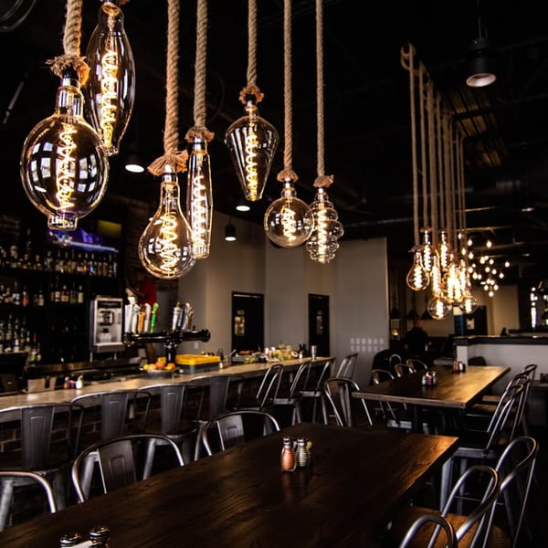 Industrial-style Edison bulb light fixtures hang above dark wood tables and a bar at Picoso's Mexican Kitchen.