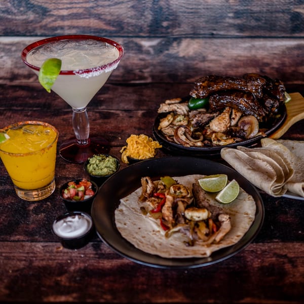 Picoso's Mexican Kitchen fajitas, ribs, and two margaritas on a rustic wooden table.