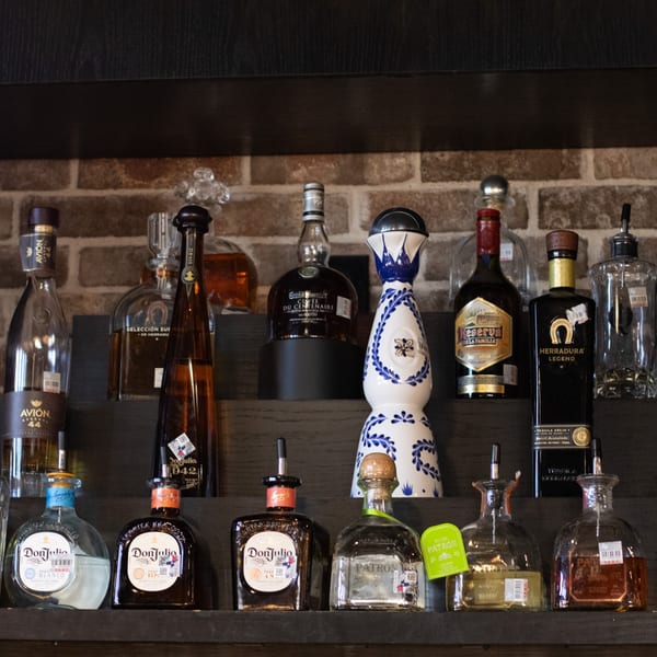 A collection of various tequila bottles, including Don Julio, Avion, and Herradura, displayed on shelves.