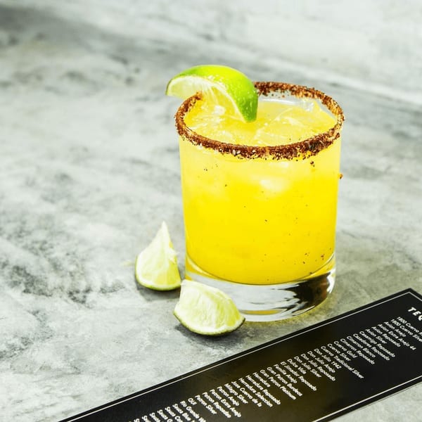 A Picoso's Mexican Kitchen margarita with a chili-lime rim and lime wedge, next to a tequila menu.