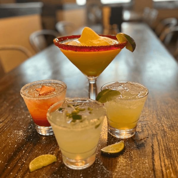 Four Picoso's Mexican Kitchen margaritas, including frozen, strawberry, jalapeño, and classic lime, on a wooden table.