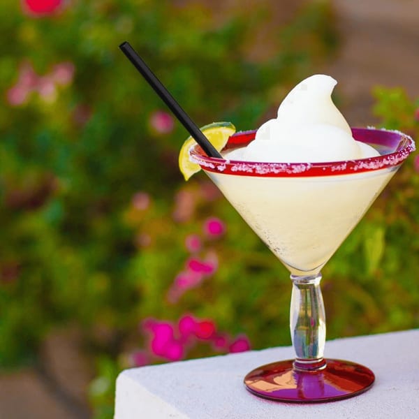 Frozen margarita with a lime wedge and red salted rim, against a blurred green and pink floral background.