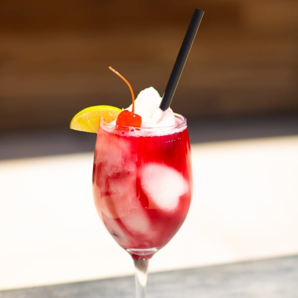 A vibrant red Picoso's Mexican Kitchen cocktail with whipped cream, a cherry, and lime.