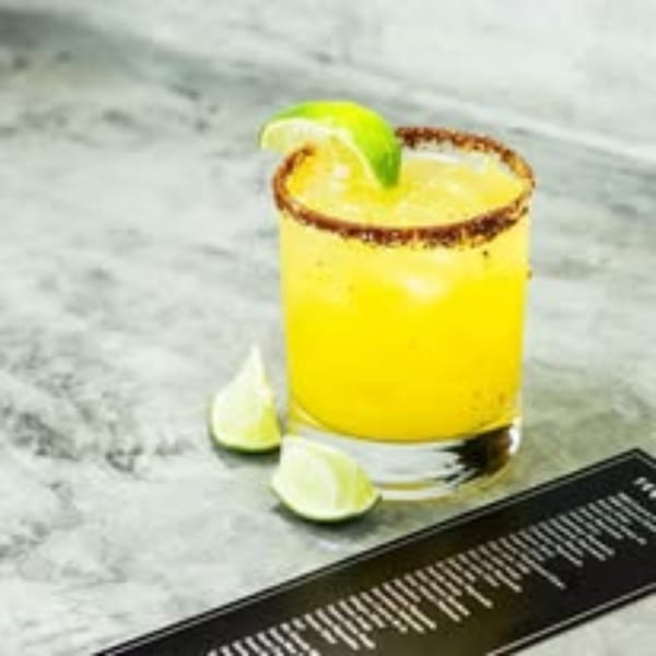 A Picoso's Mexican Kitchen margarita with a chili-lime rim and lime wedge on a gray counter.