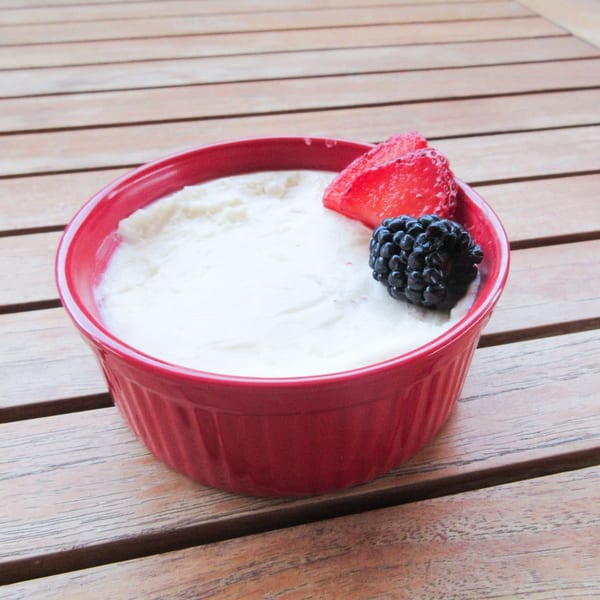 A red bowl of creamy dessert, garnished with a fresh strawberry slice and a blackberry.