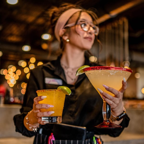 A server at Picoso's Mexican Kitchen holds two margaritas, one in a glass and one in a martini glass.