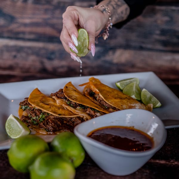 A hand squeezes lime over Picoso's Mexican Kitchen birria tacos with a side of consommé.