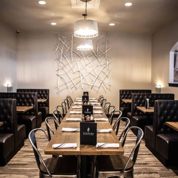 Long dining table with chairs and booths in Picoso's Mexican Kitchen, featuring modern decor.